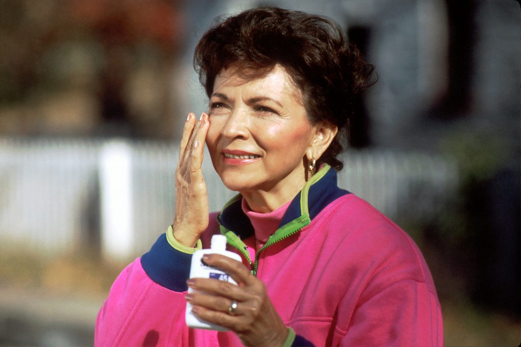 Mature woman applying sunscreen to her face outdoors on a sunny day