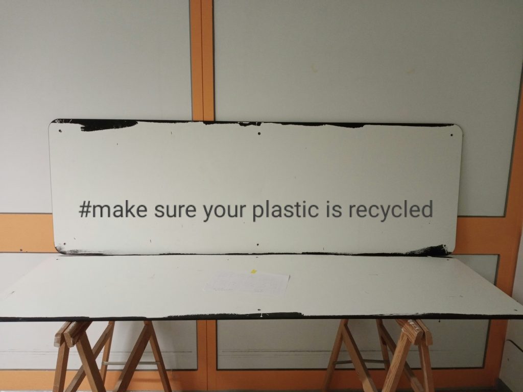 Sign on a workbench displaying the hashtag “#make sure your plastic is recycled”