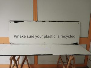 Sign on a workbench displaying the hashtag “#make sure your plastic is recycled”